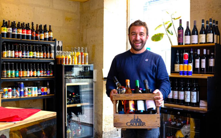 Lénaïc souriant au travail tenant un caisson à vins.