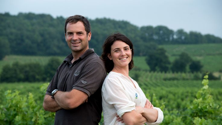 Rachel et Guillaume HUbert posant dos à dos souriants devant leurs vignes.