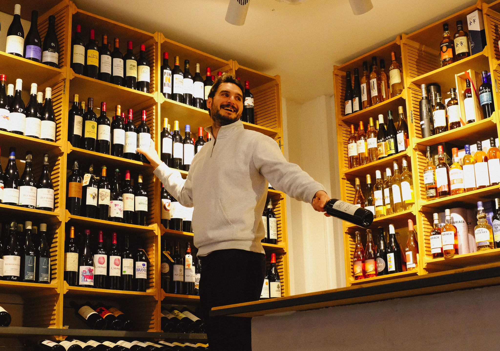 Caviste tendant une bouteille de vin a la main sur une echelle